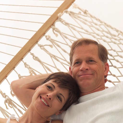 Middle-aged couple relaxes in a hammock for two; busy professionals often prefer to do their marital therapy by video via the internet to save scarce down time.